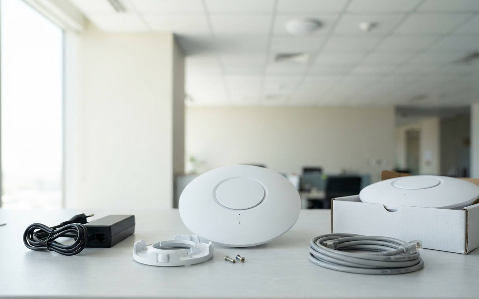 A ceiling-mount wireless access point as supplied, with its mounting bracket, PoE injector and patch lead, on a desk in a Doha office.