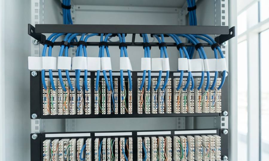 The rear of a fully terminated 24-port patch panel in an open cabinet, every pair dressed and labelled.